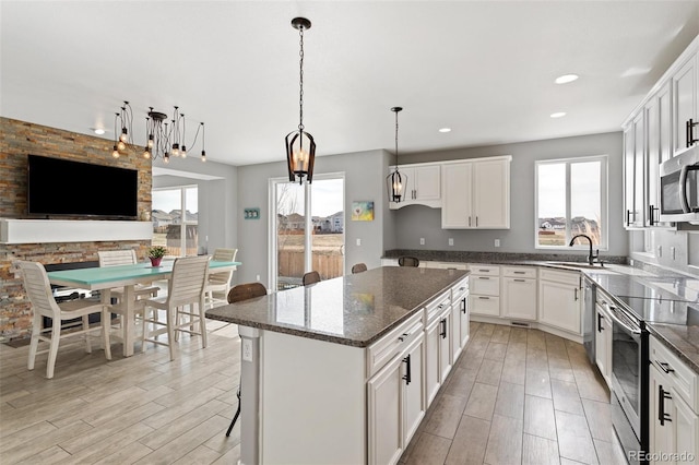kitchen with dark stone counters, stainless steel appliances, a kitchen island, a sink, and a healthy amount of sunlight