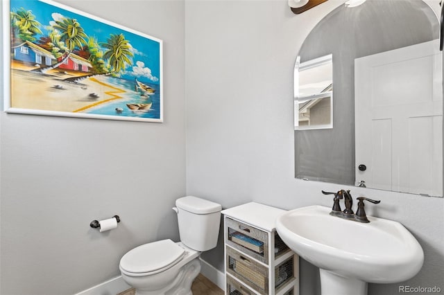 half bath with toilet, a sink, and baseboards