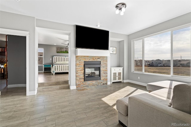 living area with baseboards, wood finished floors, a glass covered fireplace, and a ceiling fan