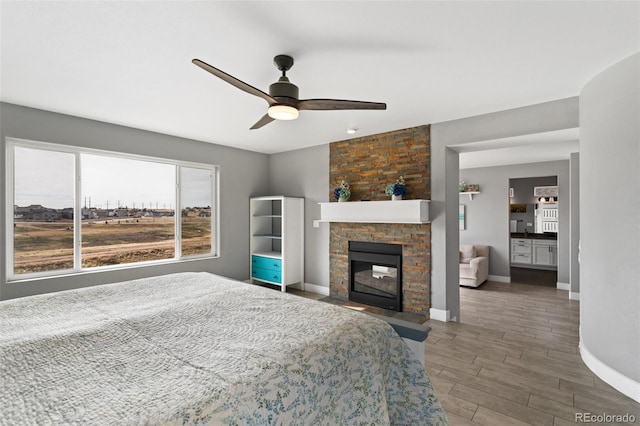 bedroom with a fireplace with flush hearth, baseboards, ceiling fan, and wood finished floors