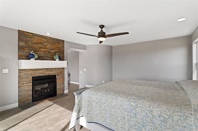 bedroom with a fireplace with flush hearth, baseboards, wood finished floors, and ceiling fan