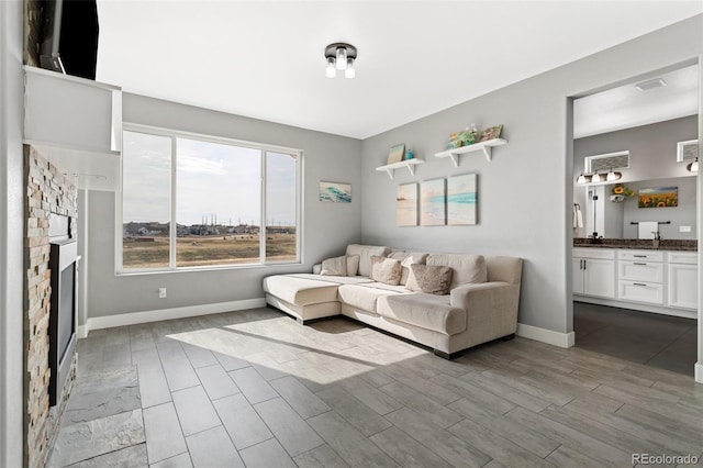living area featuring dark wood-style flooring, a stone fireplace, and baseboards