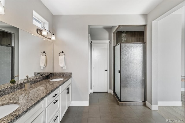 full bath featuring double vanity, a sink, a stall shower, and baseboards