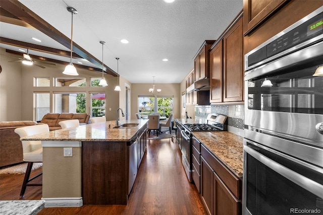 kitchen featuring a center island with sink, light stone counters, appliances with stainless steel finishes, vaulted ceiling with beams, and sink