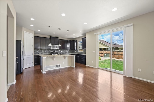 19659 W 59th Dr, Golden, CO 80403 - kitchen with appliances with stainless steel finishes, a kitchen bar, a kitchen island with sink, tasteful backsplash, and dark wood-style floors