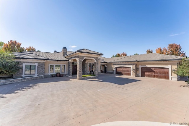 view of front of house with stone siding, concrete driveway, a garage, a chimney, and a tiled roof