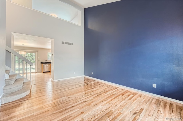 unfurnished room featuring visible vents, baseboards, light wood-style flooring, a high ceiling, and stairs