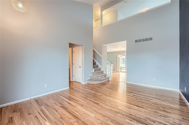 unfurnished room with a high ceiling, visible vents, baseboards, stairway, and light wood-type flooring