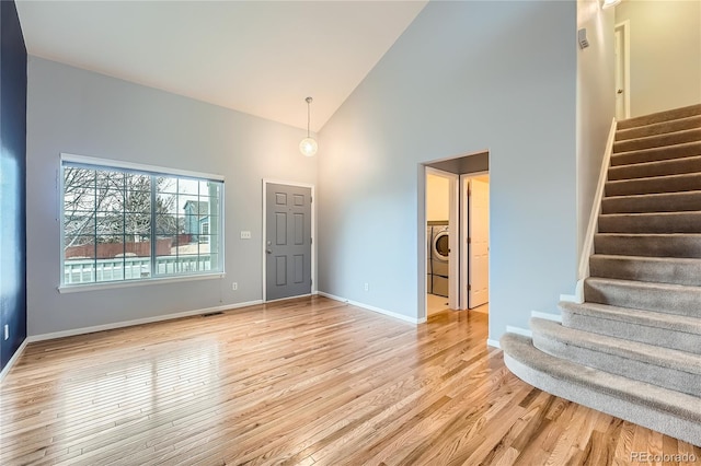 foyer featuring light wood finished floors, washer / dryer, baseboards, stairway, and high vaulted ceiling