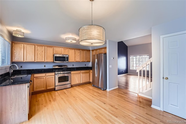 kitchen with a sink, baseboards, light wood-style floors, appliances with stainless steel finishes, and pendant lighting