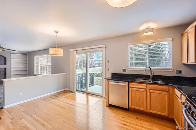 kitchen with light wood finished floors, dark stone countertops, decorative light fixtures, stainless steel appliances, and a sink