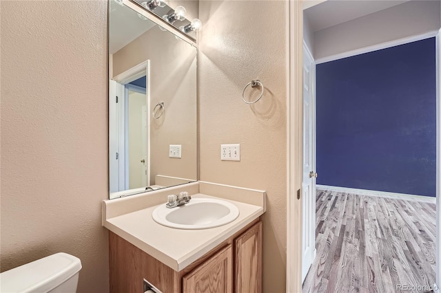 half bath featuring a textured wall, vanity, wood finished floors, and toilet