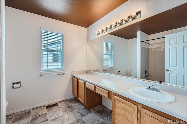 bathroom with toilet, visible vents, vanity, baseboards, and walk in shower