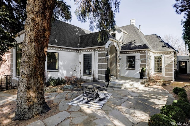 rear view of house with a chimney, a patio area, brick siding, fence, and a shingled roof