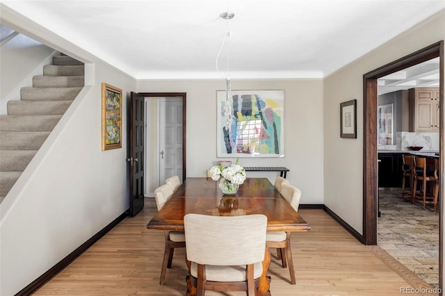 dining space with light wood finished floors, baseboards, and stairway