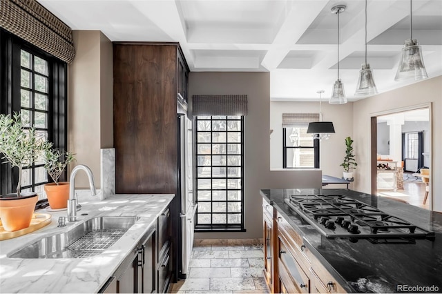 kitchen featuring light stone countertops, stainless steel gas stovetop, a sink, and pendant lighting