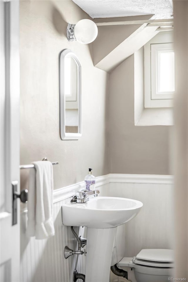 bathroom with toilet and a wainscoted wall