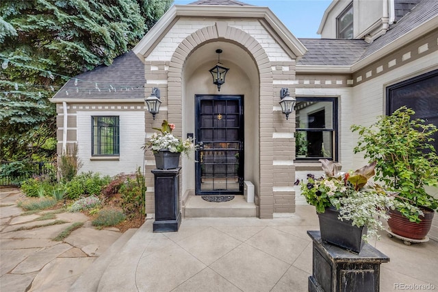 entrance to property with roof with shingles and brick siding