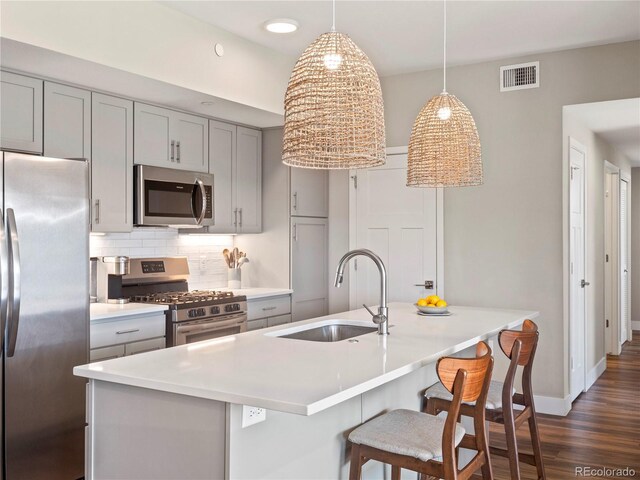 kitchen with dark wood finished floors, gray cabinets, appliances with stainless steel finishes, a sink, and decorative backsplash