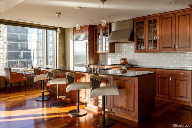 bar featuring dark hardwood / wood-style flooring, wall chimney range hood, decorative light fixtures, and built in fridge