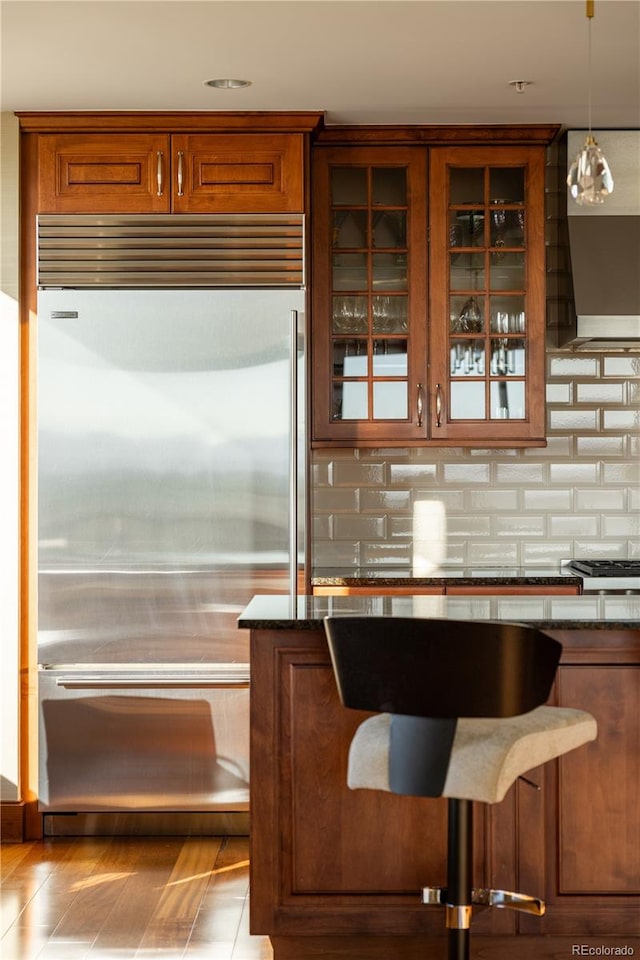 bar with light hardwood / wood-style floors, appliances with stainless steel finishes, dark stone counters, backsplash, and pendant lighting