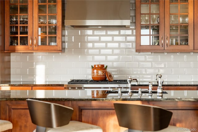 kitchen with wall chimney exhaust hood, dark stone countertops, and tasteful backsplash