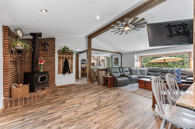 living room with hardwood / wood-style floors, vaulted ceiling with beams, a wood stove, and ceiling fan