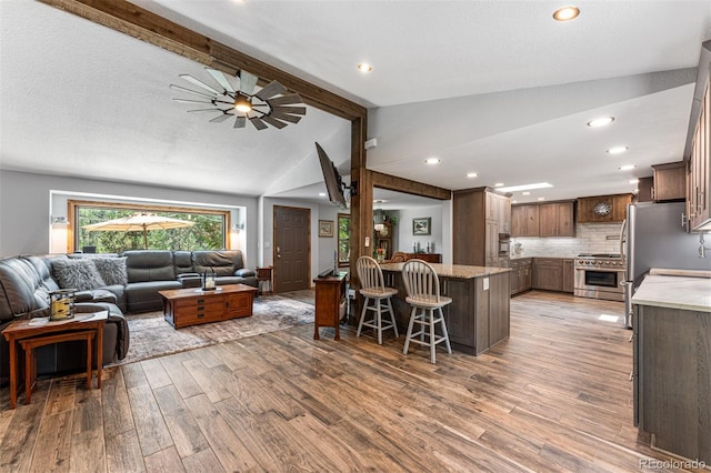 living room featuring vaulted ceiling with beams, a textured ceiling, light hardwood / wood-style floors, and ceiling fan