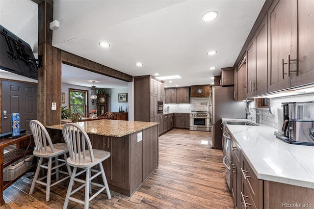 kitchen with a kitchen bar, tasteful backsplash, stainless steel stove, light stone countertops, and light hardwood / wood-style floors