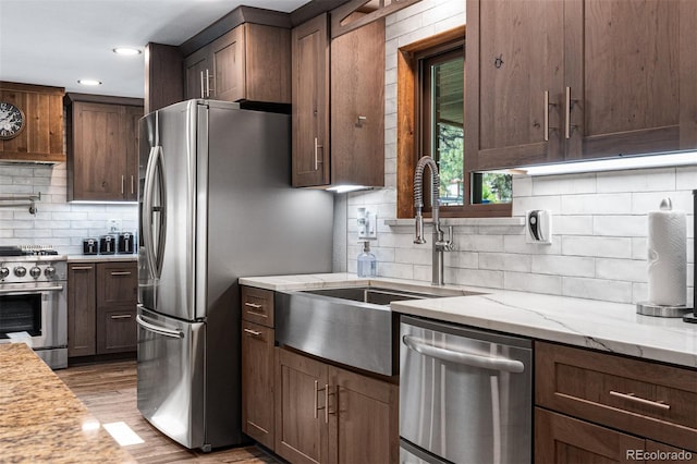 kitchen featuring tasteful backsplash, sink, light stone counters, stainless steel appliances, and light wood-type flooring