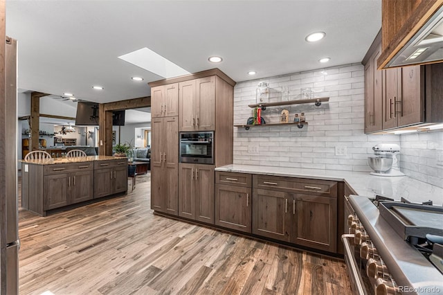 kitchen with a skylight, light hardwood / wood-style floors, stainless steel appliances, light stone countertops, and custom range hood