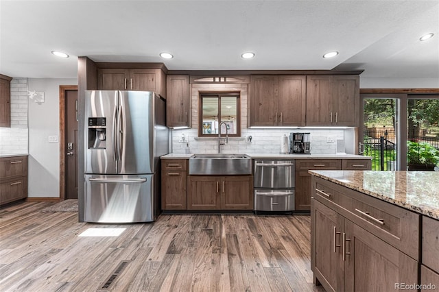 kitchen featuring sink, stainless steel fridge, hardwood / wood-style floors, tasteful backsplash, and light stone countertops