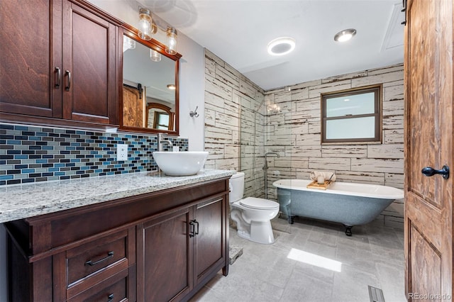 bathroom with tile walls, backsplash, vanity, a tub, and toilet