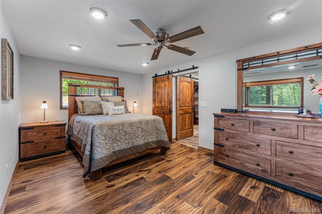 bedroom featuring a barn door, dark hardwood / wood-style flooring, multiple windows, and a textured ceiling