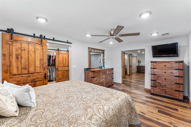 bedroom featuring dark hardwood / wood-style floors, a barn door, ceiling fan, and a spacious closet