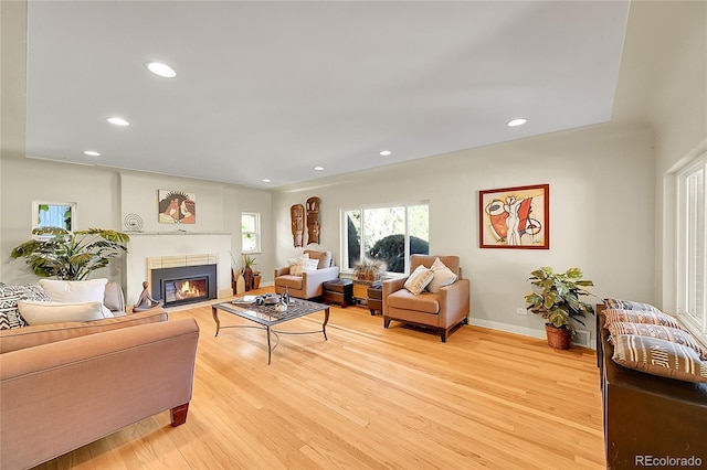 living area with light wood-type flooring, recessed lighting, a glass covered fireplace, and baseboards