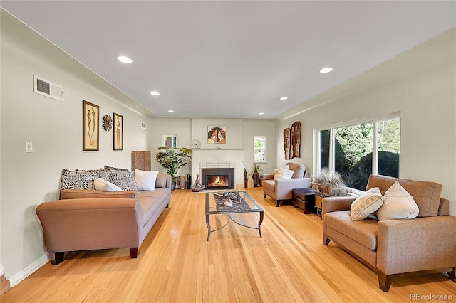 living room featuring light wood-style flooring, recessed lighting, a fireplace with flush hearth, and baseboards