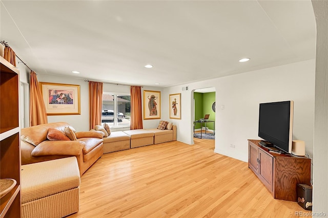 living area with arched walkways, light wood-style floors, and recessed lighting