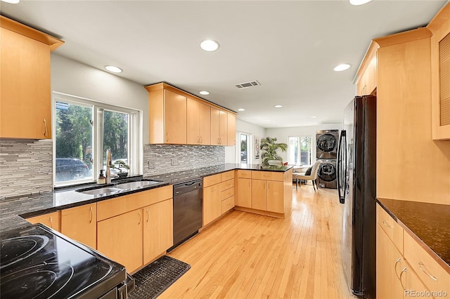 kitchen with black appliances, stacked washer / dryer, light brown cabinets, a peninsula, and plenty of natural light