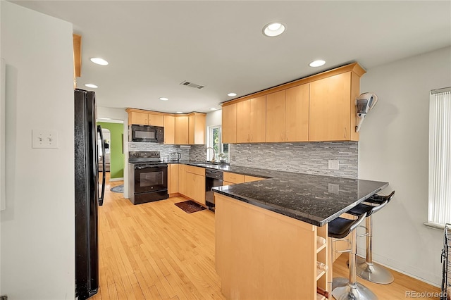 kitchen featuring black appliances, light brown cabinetry, a peninsula, a sink, and decorative backsplash