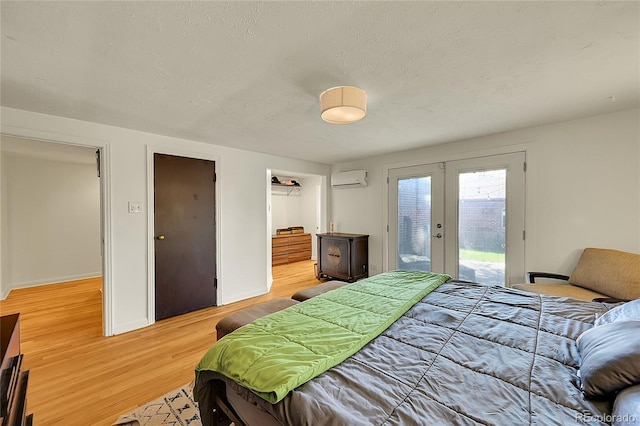 bedroom featuring french doors, a wall unit AC, access to exterior, light wood-style floors, and a textured ceiling