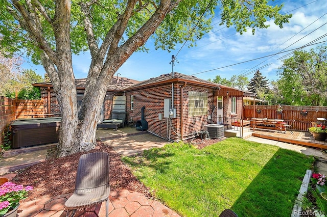 rear view of property with a deck, a patio area, a hot tub, brick siding, and central air condition unit