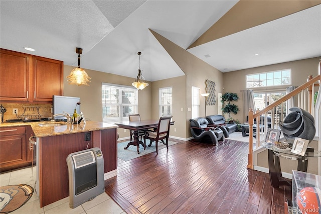 kitchen with heating unit, plenty of natural light, an island with sink, pendant lighting, and light stone countertops