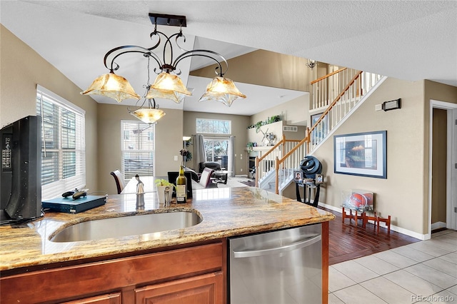 kitchen featuring light tile patterned flooring, stainless steel dishwasher, hanging light fixtures, and a textured ceiling