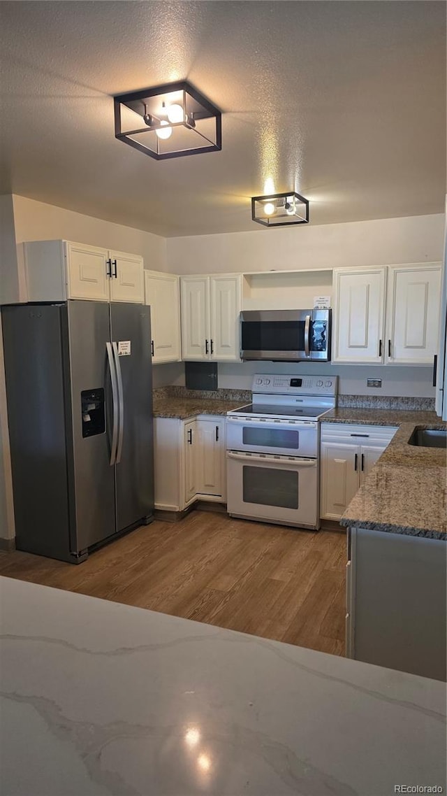 775 S Alton Way Unit 3D, Denver, CO 80247 - kitchen featuring appliances with stainless steel finishes, white cabinets, wood finished floors, and dark stone counters
