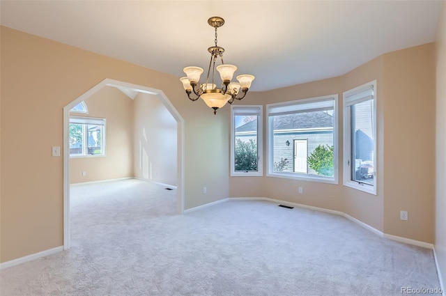 carpeted spare room with a chandelier, arched walkways, and baseboards