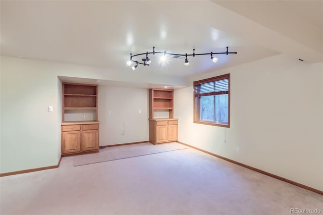 unfurnished living room featuring light colored carpet, baseboards, rail lighting, and built in shelves