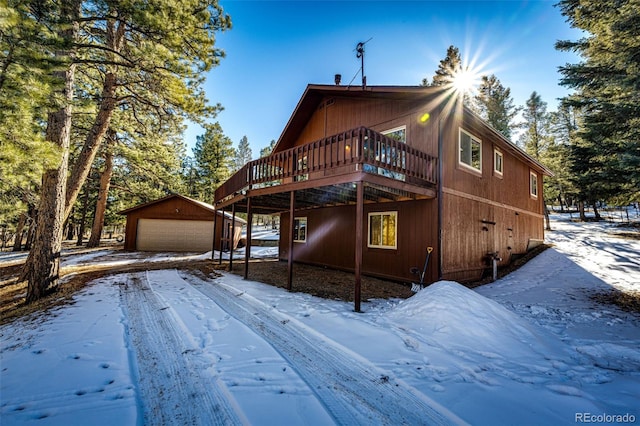 view of snow covered exterior with a garage, an outbuilding, and a deck