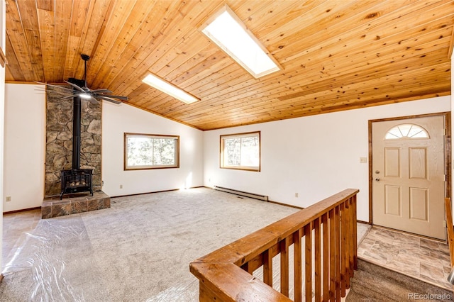 unfurnished living room featuring lofted ceiling with skylight, a baseboard radiator, carpet flooring, a wood stove, and wooden ceiling