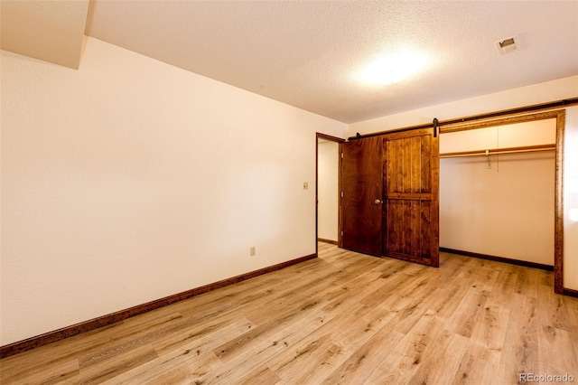 unfurnished bedroom featuring a barn door, a textured ceiling, light hardwood / wood-style floors, and a closet